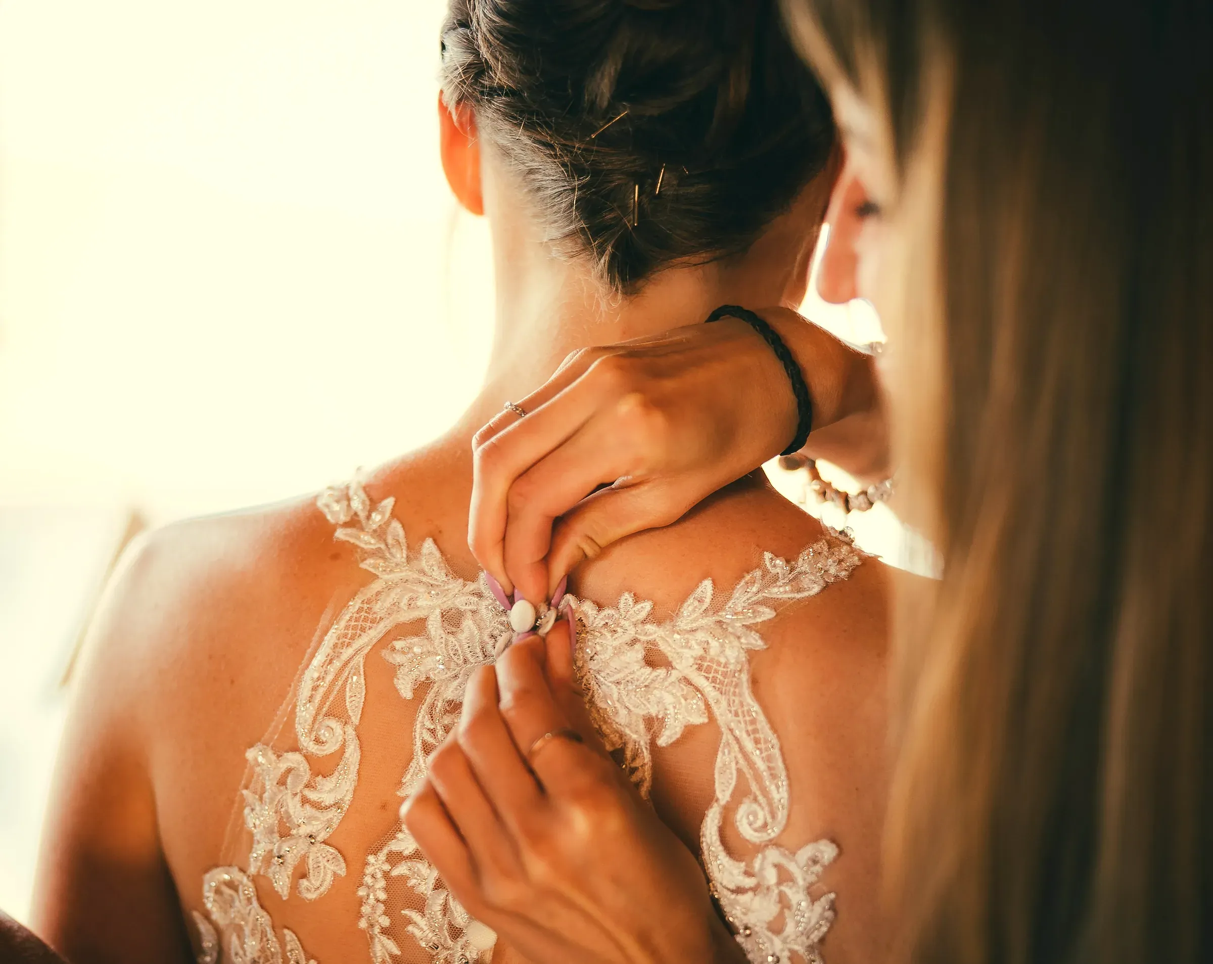 La sposa di spalle, il pizzo, la mano all'orecchino