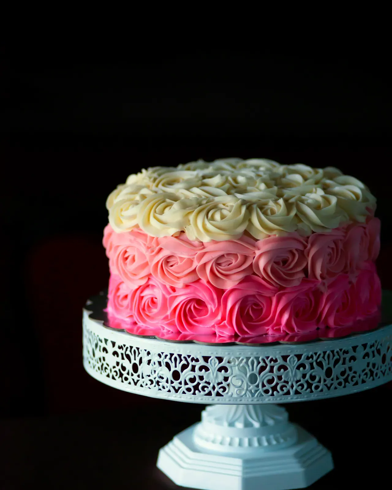 La torta a rose di crema, sfumata dal rosa al bianco, sull'alzata