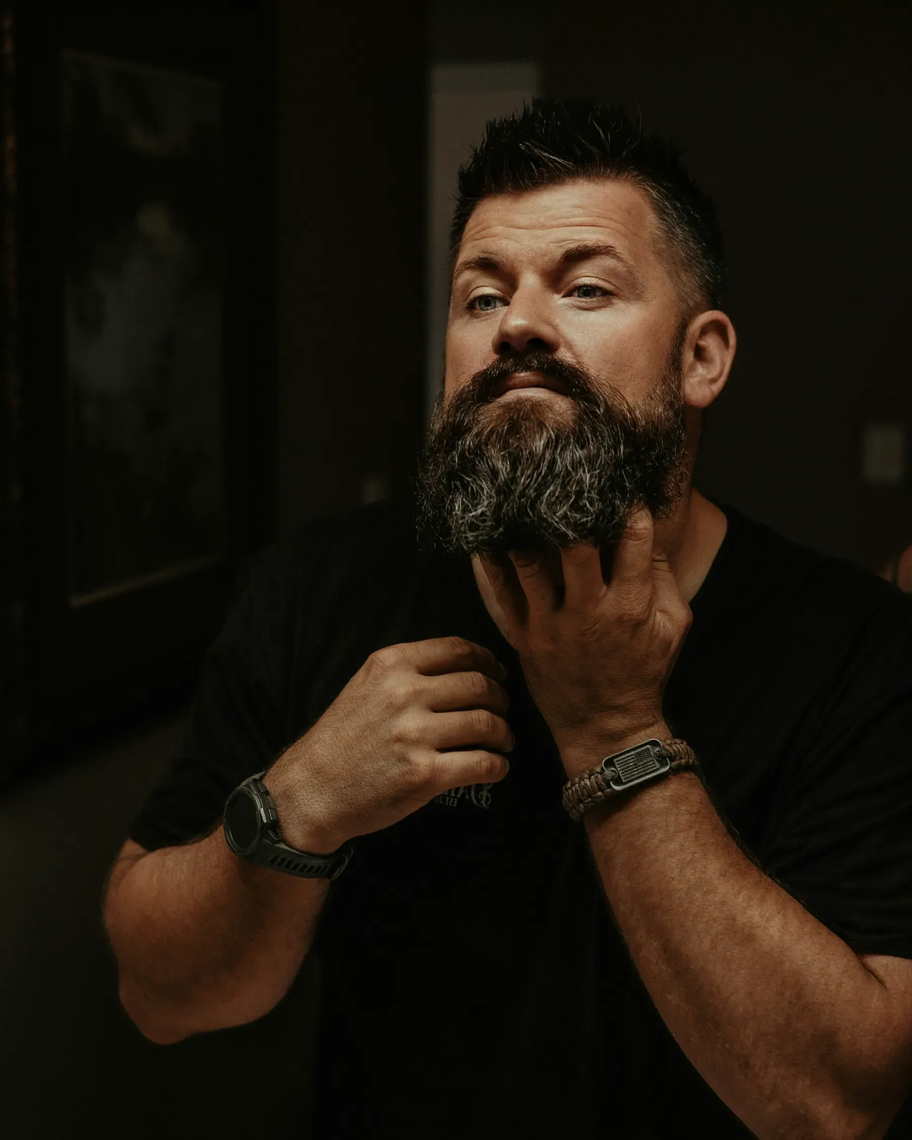 La mano sulla barba piena e curata, nella penombra