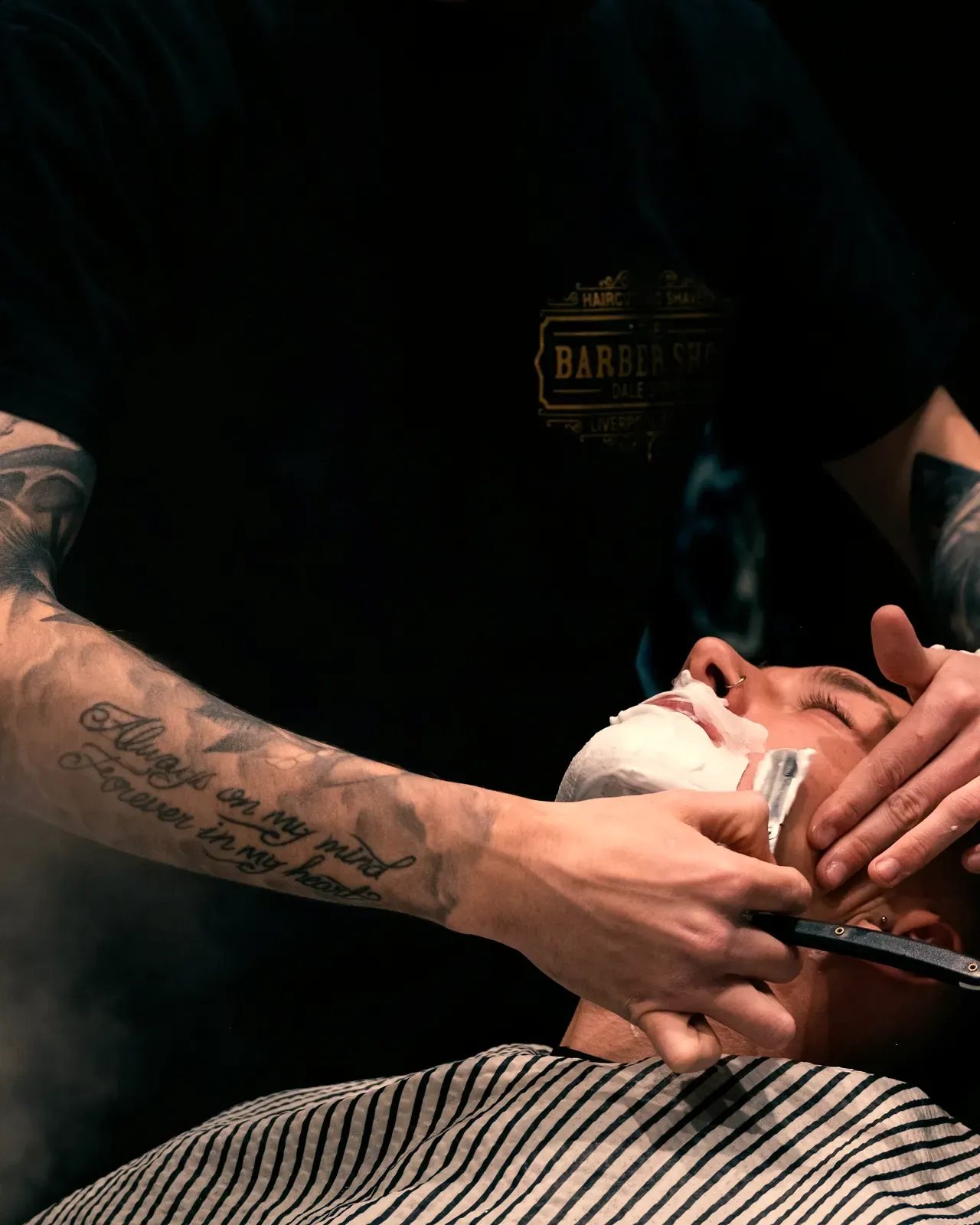 Le mani del barber con il rasoio sul viso insaponato, il vapore del panno