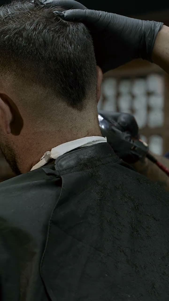 Le mani del barber con il pettine e le forbici sulla nuca, nel buio