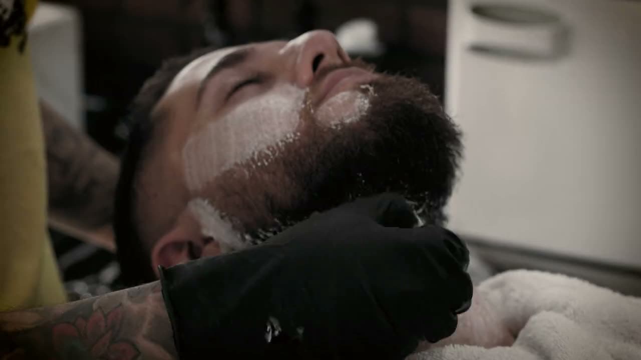 La schiuma sulla barba e le mani del barber con i guanti, prima della lama
