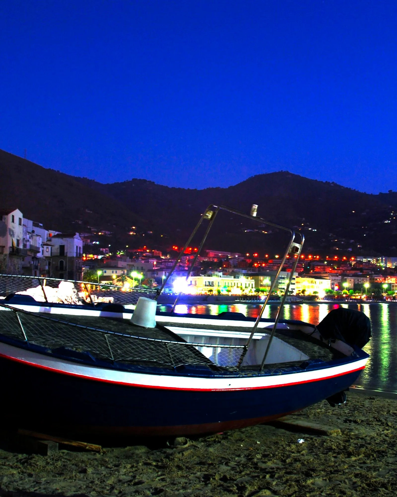 Il porto vecchio la sera: una barca sulla sabbia, le luci del paese sull'acqua