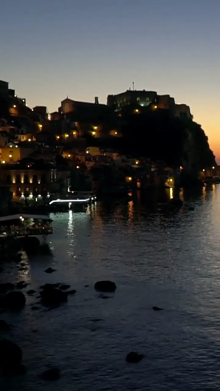Il paese sulla roccia al tramonto, le luci accese, il mare fermo sotto