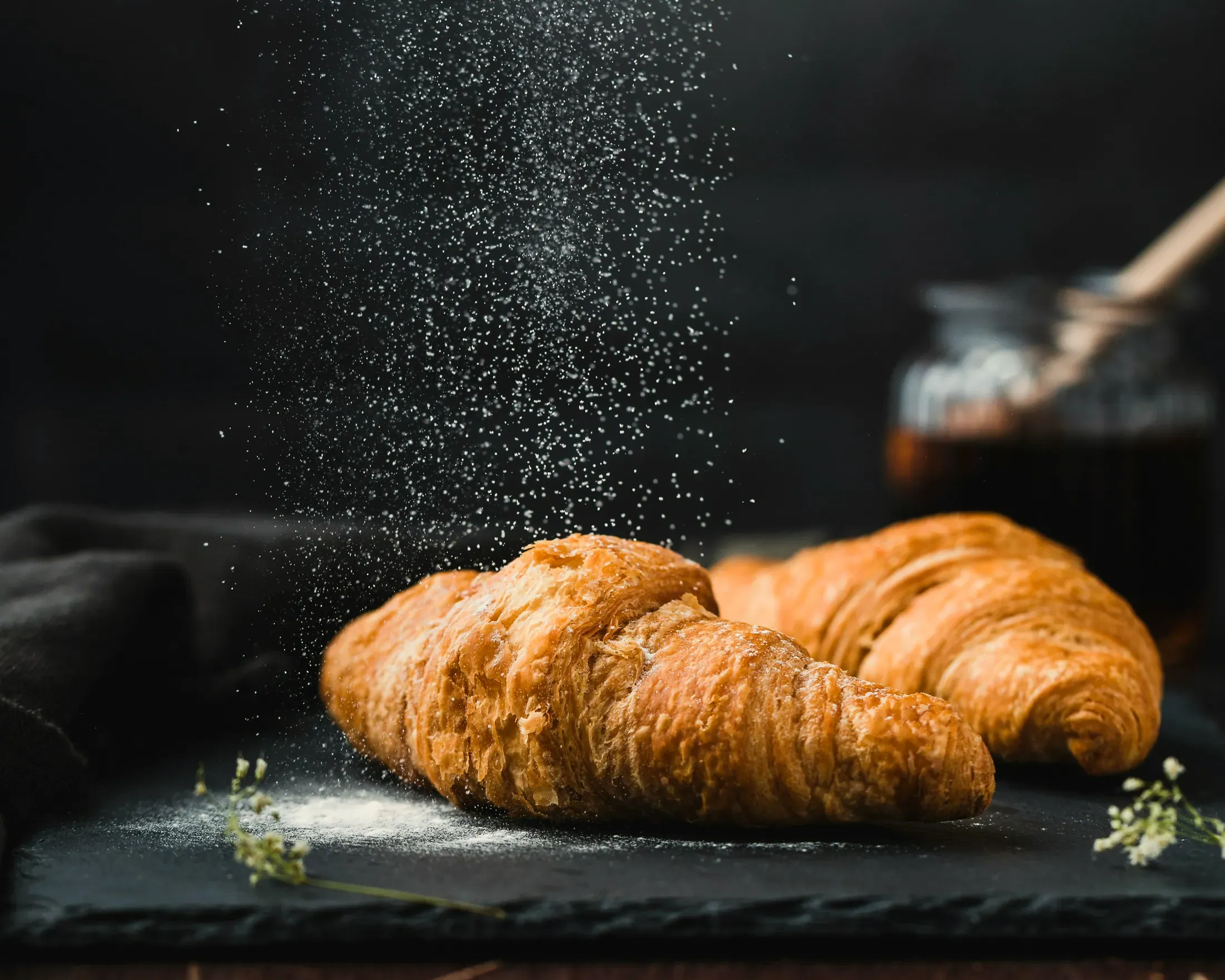 Il croissant con lo zucchero a velo che cade, su fondo scuro